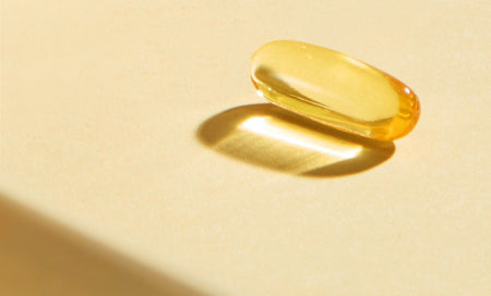 Golden translucent supplement capsule on warm beige surface, highlighting purity and daily wellness support