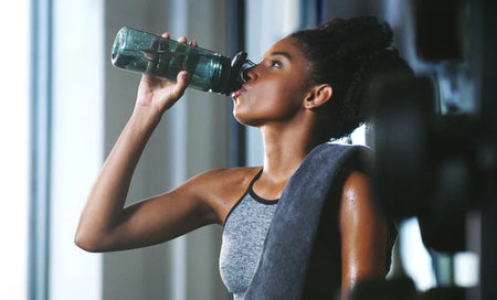 Woman drinking water from bottle after workout, promoting daily wellness and hydration