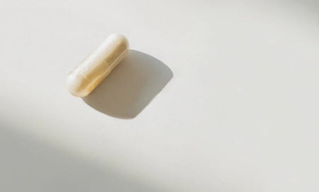 Beige supplement capsule on white surface with soft shadow, science-backed daily wellness