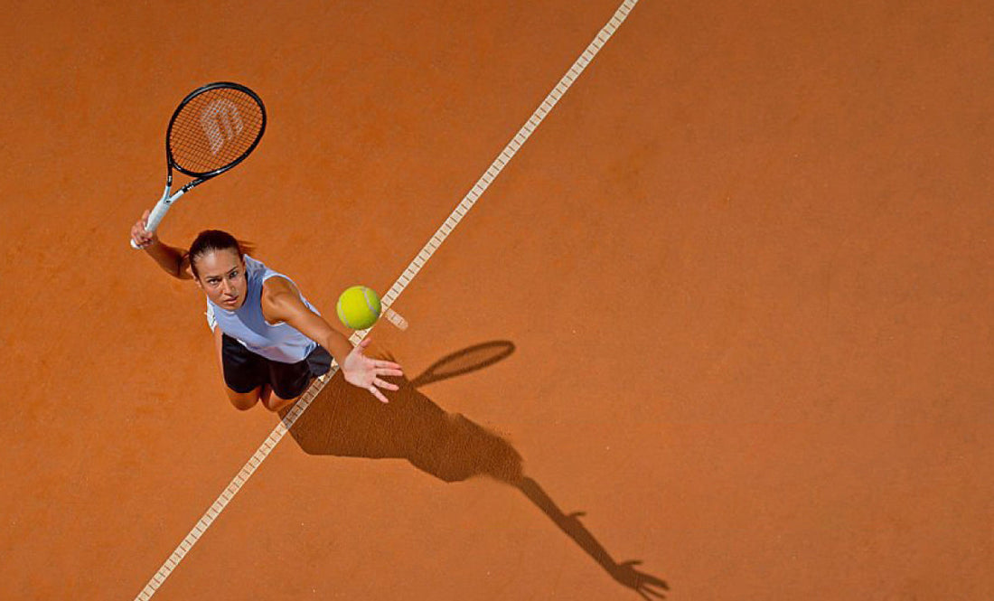 Female tennis player serving on clay court with racket and ball in action